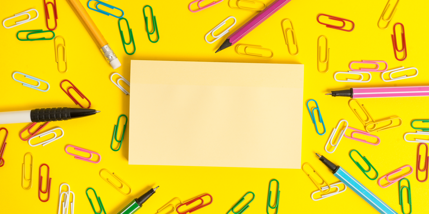 canva In der Mitte liegt ein Notizzettel, um diesen Zettel liegen Büroklammern und vier Stifte
